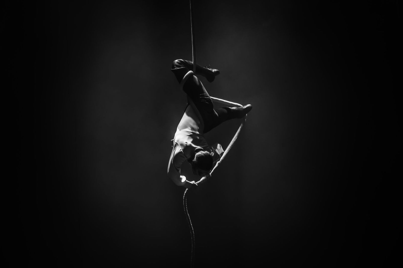 Acrobate suspendu à un mât dans une lumière théâtrale